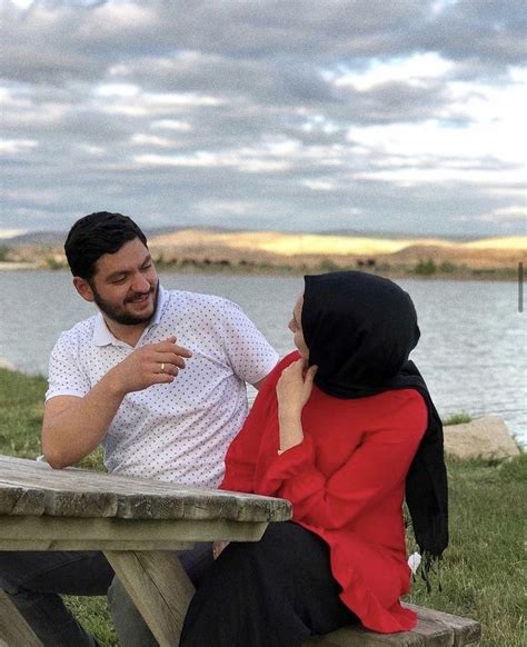 A Man And Woman Sitting At A Picnic Table Next To The Water Looking At