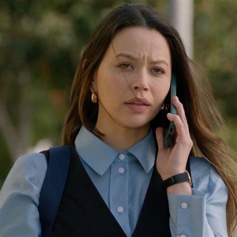 a woman talking on a cell phone while wearing a blue shirt and black vest,