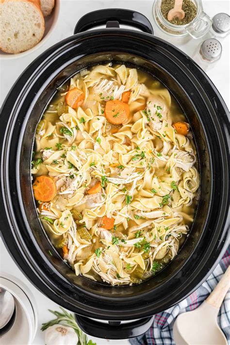 A Crock Pot Filled With Chicken Noodle Soup On Top Of A White Table