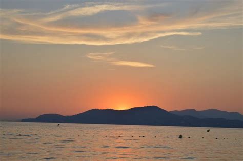 The Sun Is Setting Over The Water With Mountains In The Background