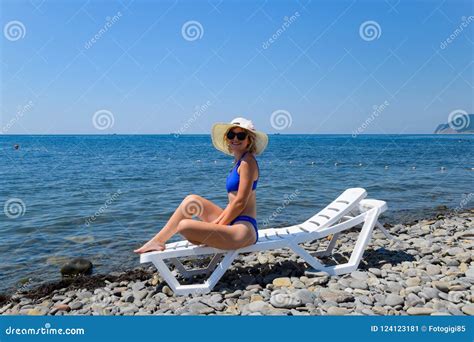 Beautiful Girl In A Blue Bikini And White Hat Sunbathing On The Beach