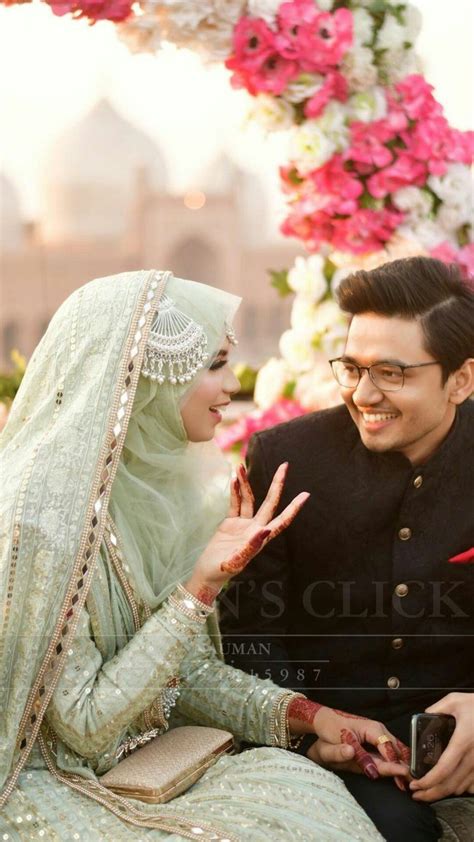 A Man And Woman Sitting Next To Each Other In Front Of A Flower Covered