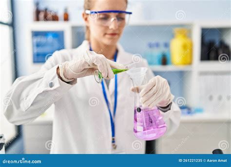 Young Blonde Woman Wearing Scientist Uniform Pouring Liquid On Test Tube At Laboratory Stock