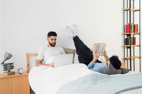 Jeune Couple Gay Coucher Lit Lire Livre Et Téléphone Portable Photo Gratuite