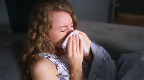 Woman Sick With Flu Coughs And Blows Her Nose Under Blanket On Couch At