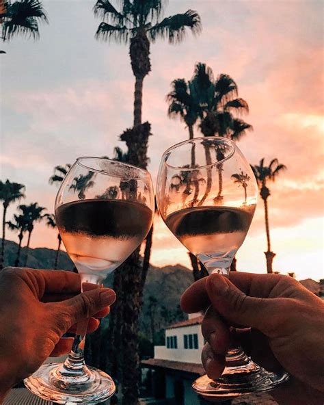 Two People Toasting With Wine Glasses In Front Of Palm Trees At Sunset