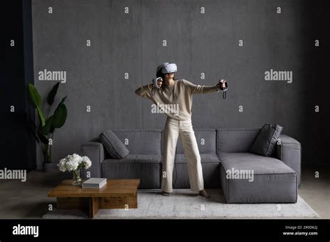 A Woman In Virtual Reality Glasses With Joysticks In Her Hands Sitting On A Couch And Traveling