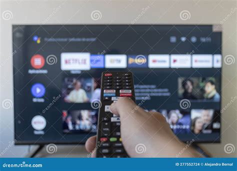 A Male Hand Holding A Remote Control With Android Tv Interface