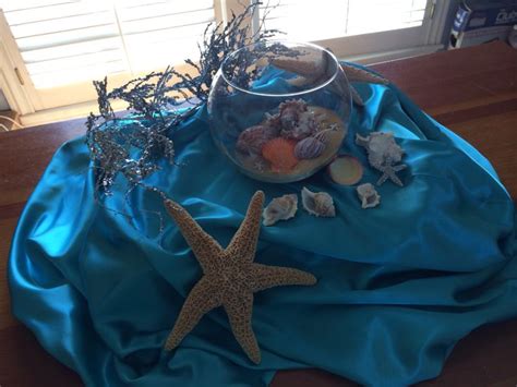 A Starfish Sits On A Blue Cloth Next To A Bowl Filled With Sea Shells