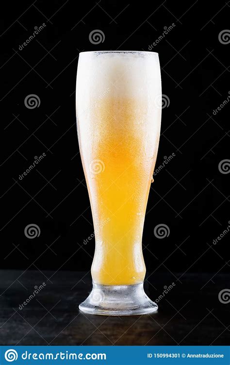 Glass Of Fresh Cold Light Beer With Froth Flowing On The Table And Beautiful Spilled Beer On A