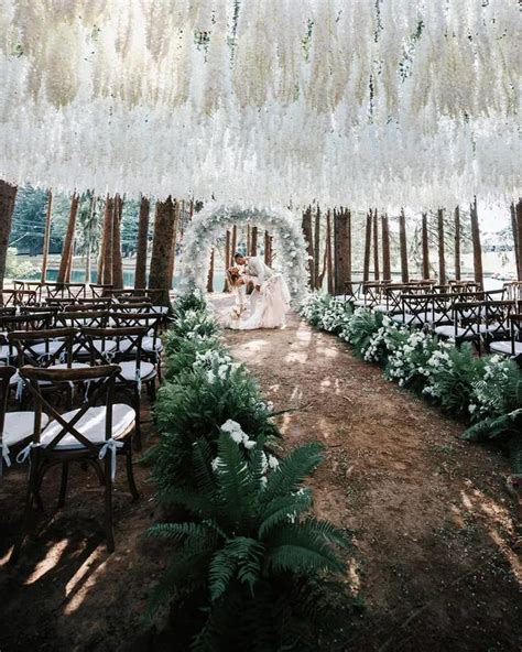 An Outdoor Ceremony With White Flowers And Greenery Hanging From The