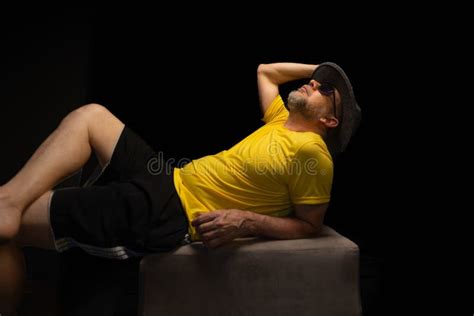 Mature Man 50s Quite Uninhibited With A Beard And Sunglasses Wearing A Hat And Yellow Shirt