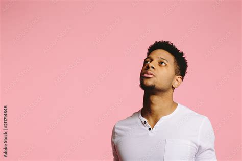 Close up portrait of a young man looking up and left with interest, , isolated on pink studio ...