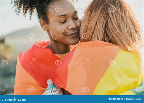 Loving Multiethnic Lesbian Couple Wrapped In Flag Hugging Outdoors