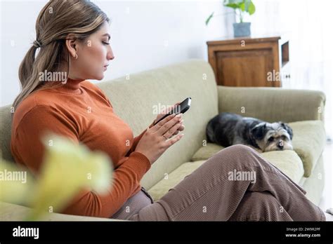 Jeune fille latine blonde assise sur un canapé de salon avec son téléphone portable à côté de