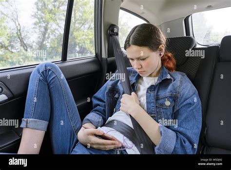 Teen Girl Sitting In Car In Back Passenger Seat With Smartphone And