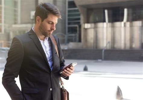 Un hombre con traje mira su teléfono mientras está parado afuera