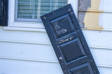 A Black Broken Window Shutter Barely Hanging Onto The Wall Stock Photo