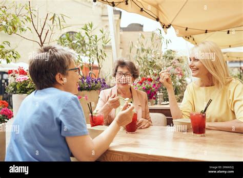 Smiling Mature Women Sitting In Cafe Terrace Drinking Coffee And