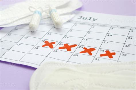 Menstrual Pads And Tampons On Menstruation Period Calendar With Red Cross Marks Lies On Lilac