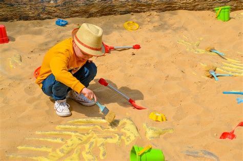 Un niño con sombrero de paja dibuja en la arena con un cepillo Foto