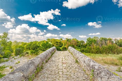 Rock Stone Bridge Across Small Pond With Green Trees Under Blue Sky