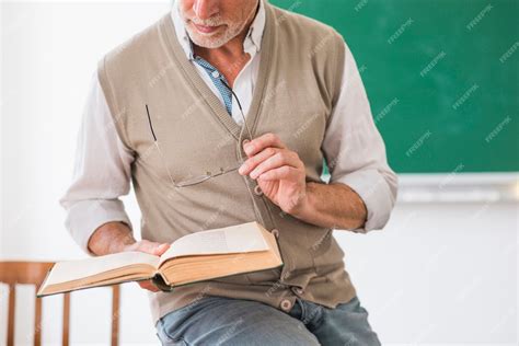 Free Photo Senior Male Professor Holding Book And Glasses In Classroom