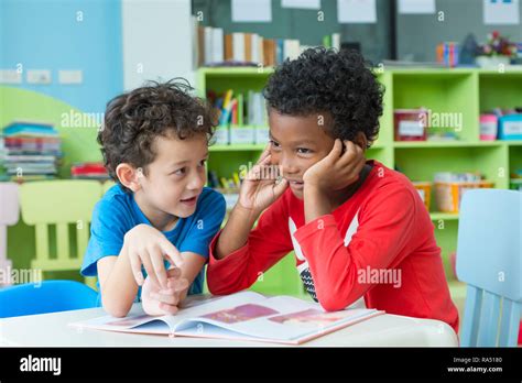 Two Boy Kid Sit On Table And Reading Tale Book In Preschool Library