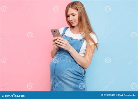 Happy Young Pregnant Woman Using A Mobile Phone Looks At The Smartphone