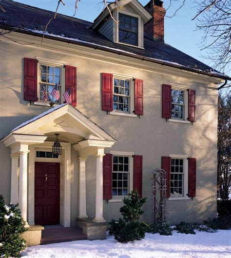 A Large White House With Red Shutters And Snow On The Ground In Front Of It