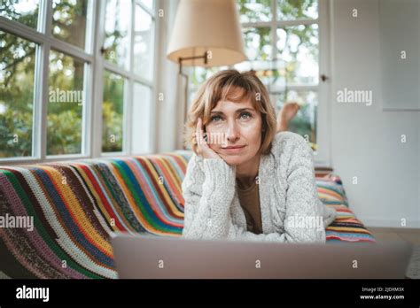 Thoughtful Mature Woman With Laptop Lying On Sofa At Home Stock Photo Alamy