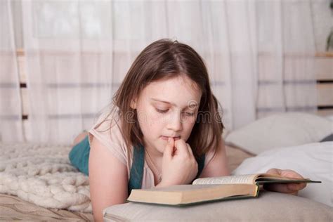 Adolescente Acostada En La Cama Y Leyendo Un Libro Imagen De Archivo