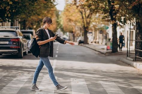 Mujer joven cruzar la calle y utilizar teléfono Foto Gratis