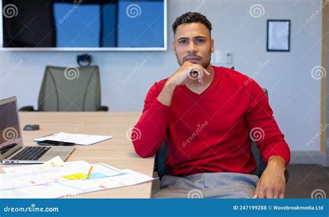 Portrait Of Hispanic Businessman With Hand On Chin By Documents At