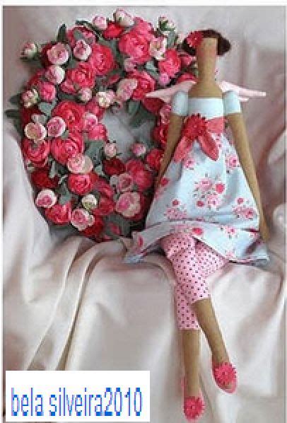 A Doll Laying On Top Of A White Sheet Next To A Pink Flowered Wreath