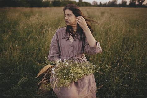 바람이 부는 머리와 린넨 드레스를 입은 아름다운 여자가 여름 초원에서 꽃다발과 함께 나무 의자에 앉아 있다 저녁 시골에서