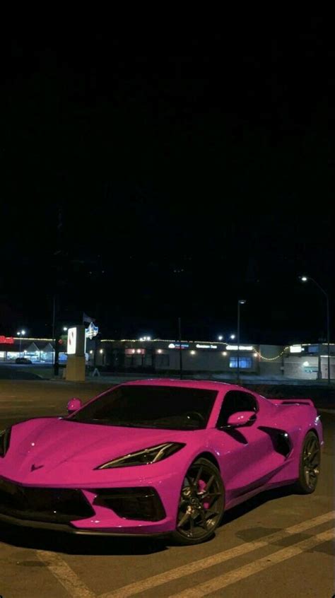 A Pink Sports Car Is Parked In A Parking Lot At Night With Its Lights On