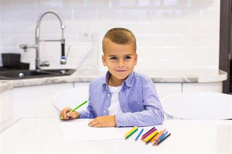 Garotinho Se Senta Em Uma Mesa Em Uma Cozinha Brilhante E Desenha