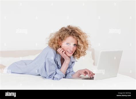 Gorgeous Blonde Female Relaxing With Her Laptop While Lying On Her Bed In Her Appartment Stock