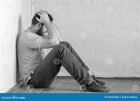 A Man With A Beard Is Sitting In The Corner Of The Room With His Head