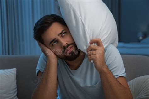 Unhappy Young Man Covering Ears In Living Room At Night Noisy