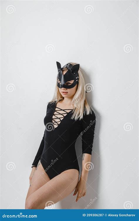 Cute Blonde Woman In Leather Mask And Black Bodysuit Stands And Poses In Studio Stock Image