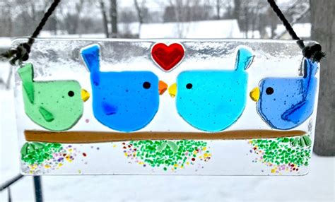 A Glass Bird Feeder With Three Birds On Its Side And A Heart In The Background