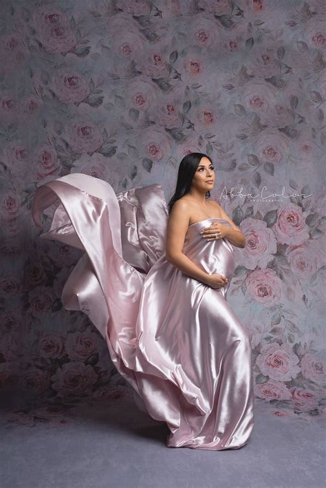 A Pregnant Woman In A Pink Gown Poses For A Photo Against A Floral