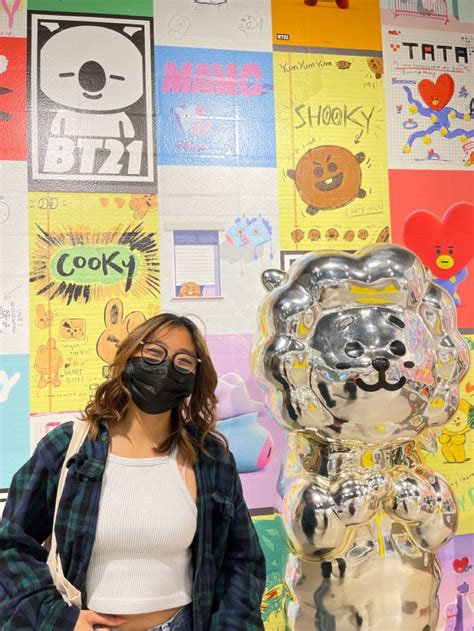 A Woman Wearing A Mask Standing In Front Of A Wall Covered With Posters