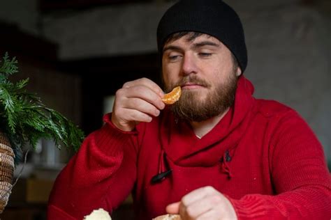 Premium Photo A Man In A Hat And Sweater Eats A Tangerine