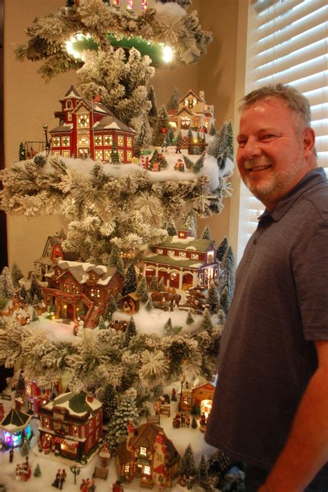 A Man Standing In Front Of A Christmas Tree That Has Snow On It And Houses