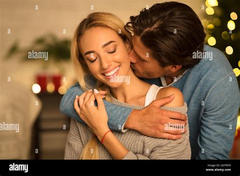 Man Kissing Neck Of Stunning Woman Sitting Near Christmas Tree Stock