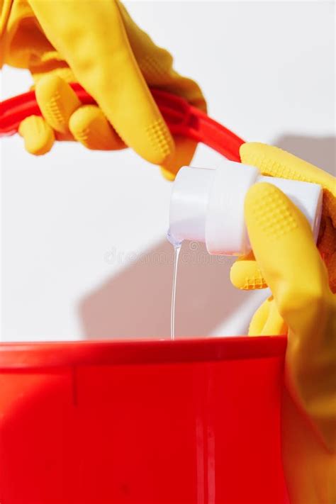 Woman In Yellow Rubber Gloves Holding Red Bucket And Bottle Of Hand