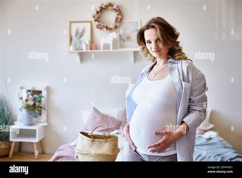 Cute Pregnant Girl Is Standing In The Bedroom Near The Bed And Looking At The Camera Gently